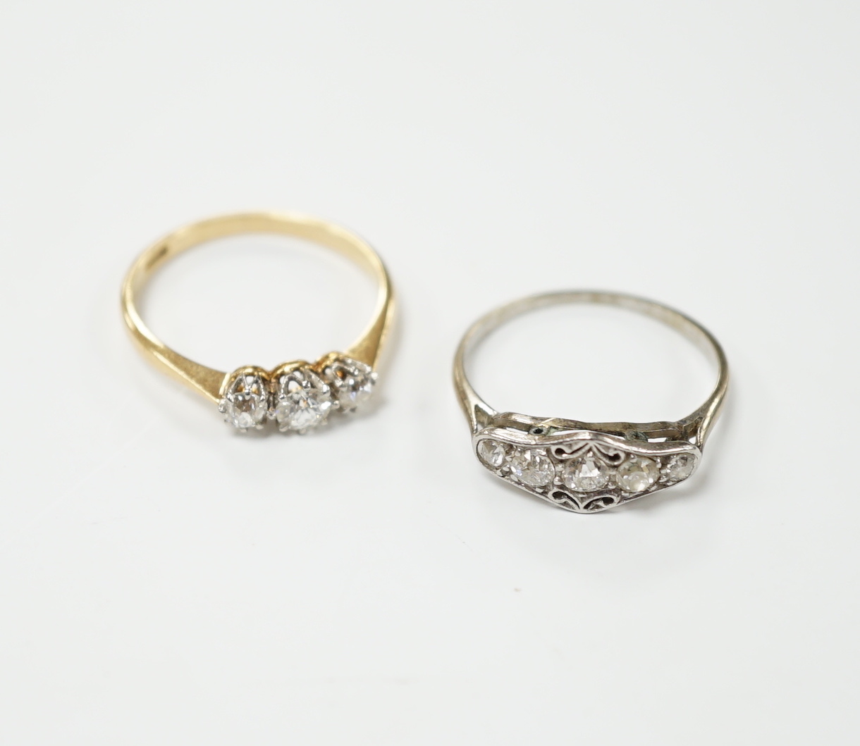 An 18ct gold three stone diamond ring, size M and a white metal five stone diamond dress ring, size M